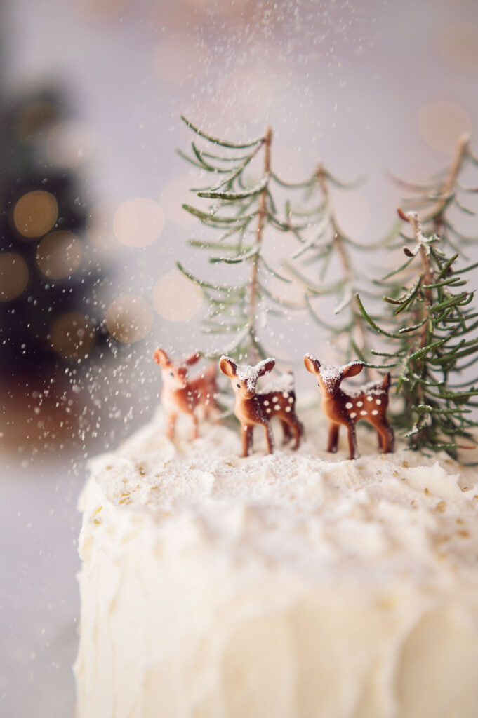 powdered sugar snow on deer miniatures on top of a white cake