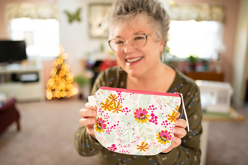 Smiling woman holds a floral printed zipper bag with a hot pink zipper