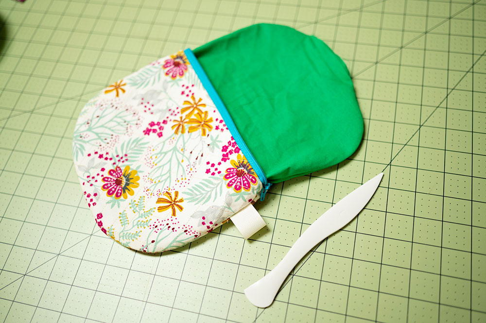 quilted zipper pouch is sewn and turned right side out. Laying on a cutting mat and shown with the point turner tool