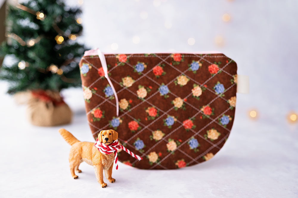 a golden retriever miniature posed with a floral zipper pouch