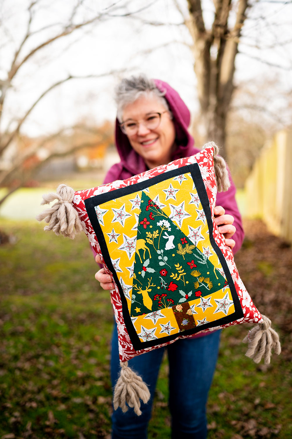 smiling woman holds a complete Christmas tree quilt block sewn into a pillow