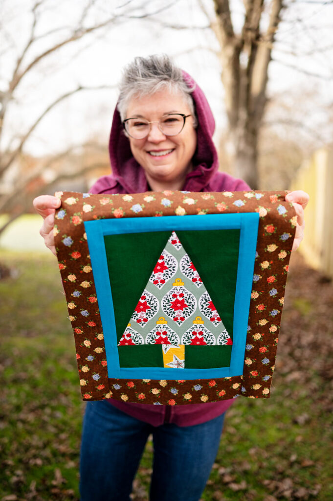 smiling woman holds a complete Christmas tree quilt block