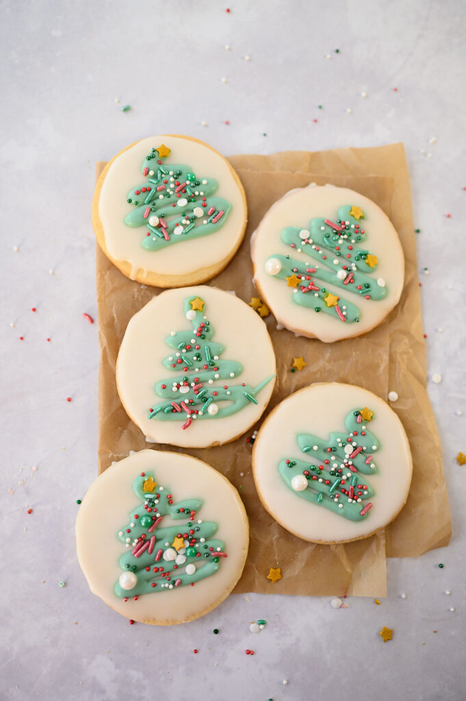 overhead view of 4 round Christmas cookies decorated with green trees and seasonal sprinkles