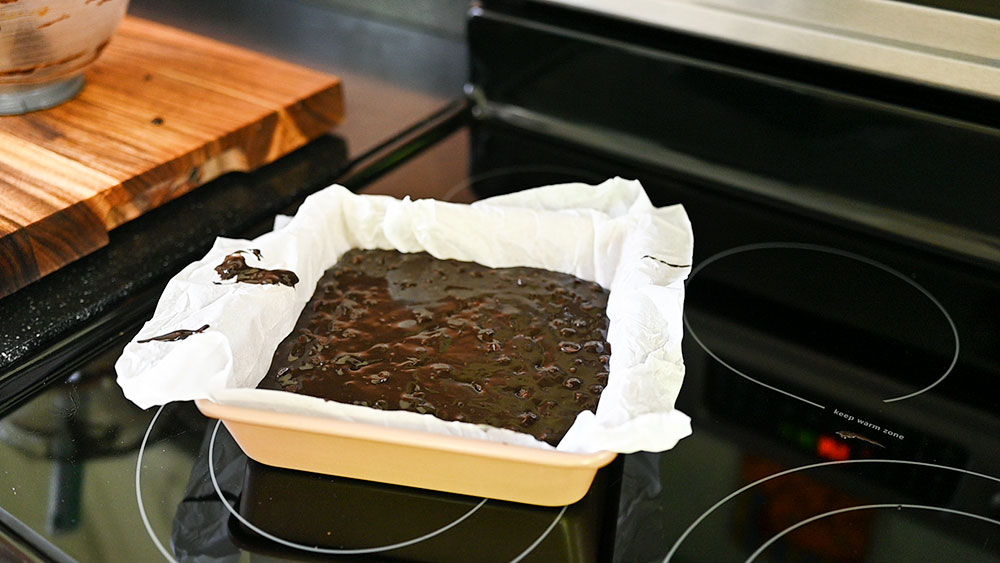 a parchment lined pan is filled with brownie batter and ready to be baked