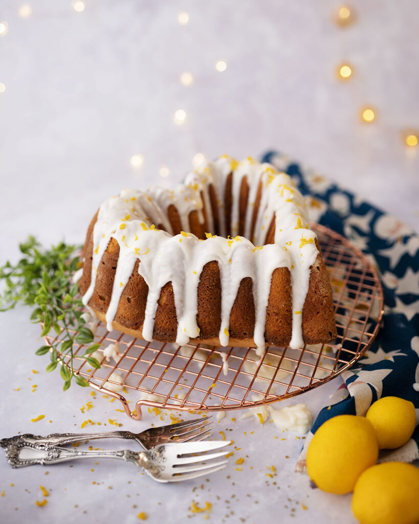 lemon bundt® cake with glaze posed with meyers lemons and antique silver ware