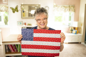 smiling woman holds an placemat that looks like an American Flag