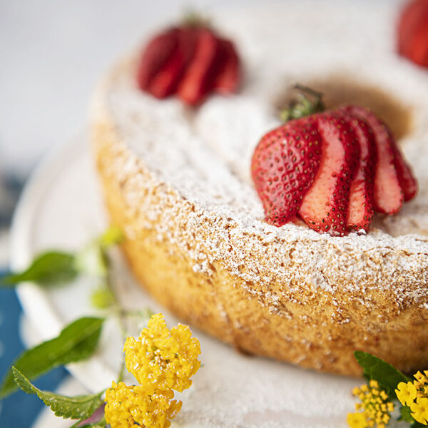 an angel food cake topped with powdered sugar and sliced strawberries with fresh picked yellow flowers