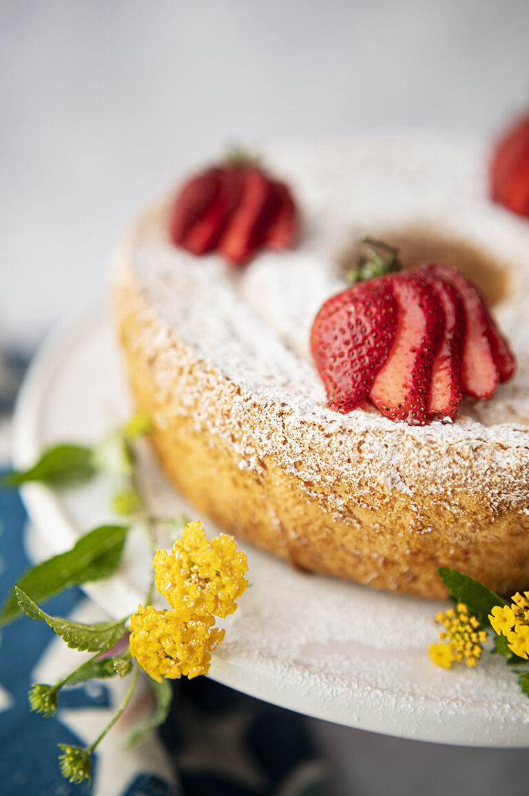 an angel food cake topped with powdered sugar and sliced strawberries with fresh picked yellow flowers