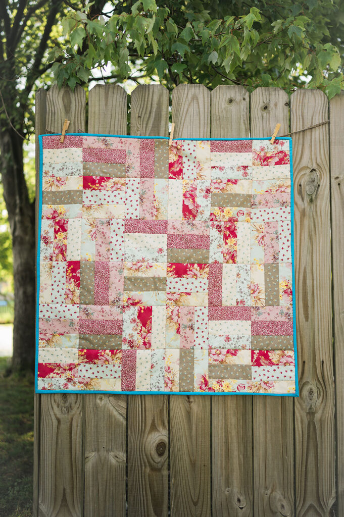 a square patchwork quilt hanging on a rustic fence