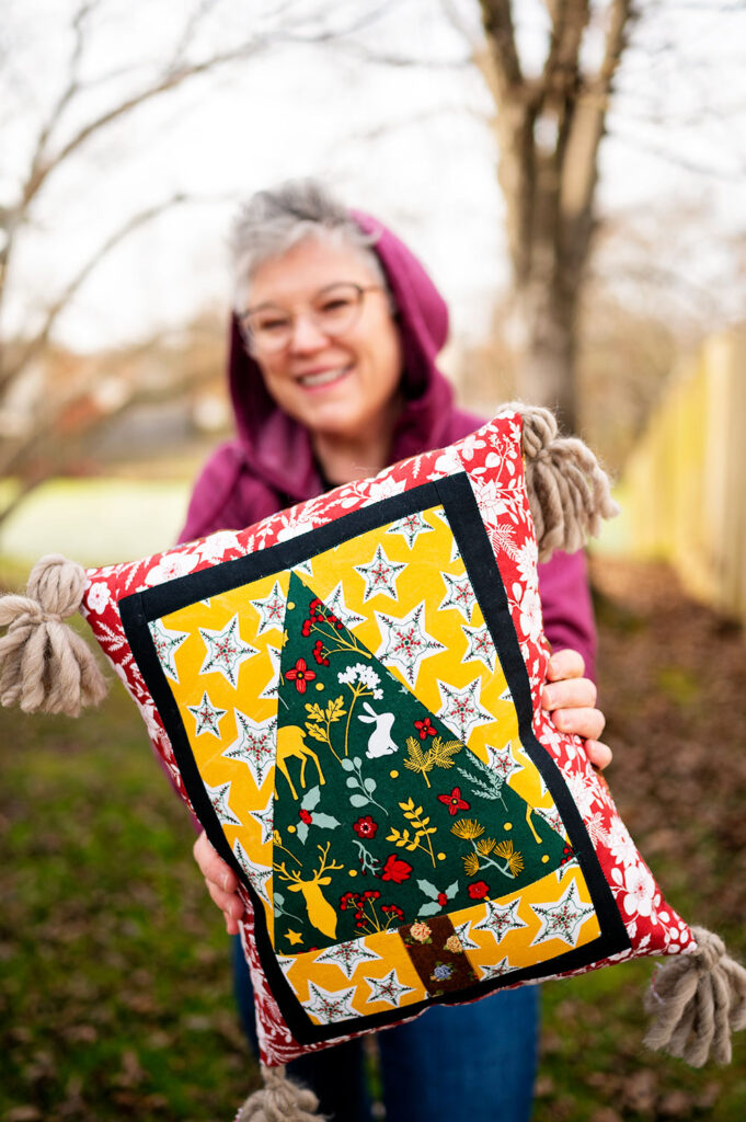 a woman holding a finished quilted pillow