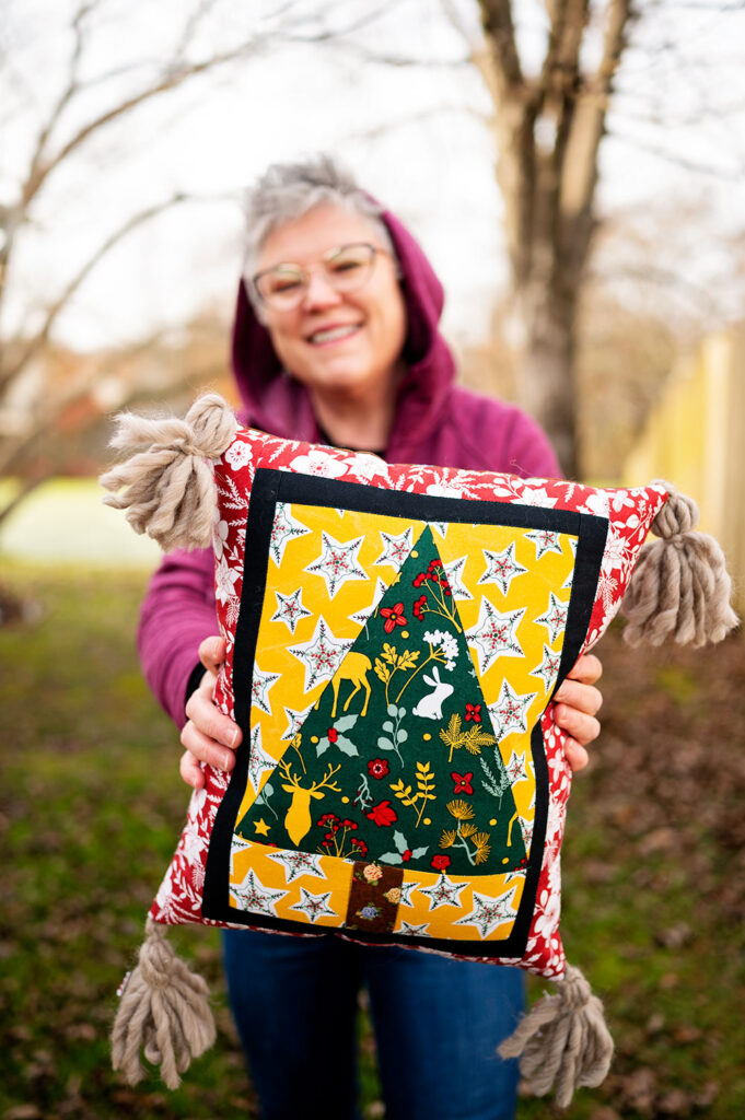 smiling woman holds a pretty quilted pillow