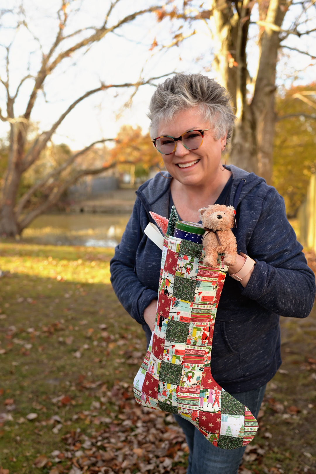 a smiling woman holds a patchwork Christmas stocking