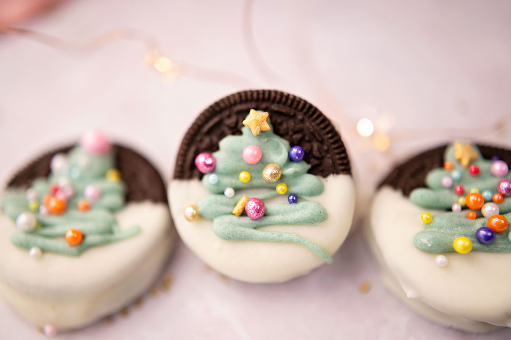 three decorated oreo cookies dipped in white chocolate and decorated with sprinkles to look like a Christmas tree