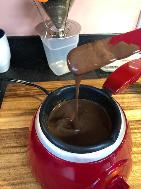melted chocolate in a chocolate pot with a dipped utensil demonstrating proper consistency