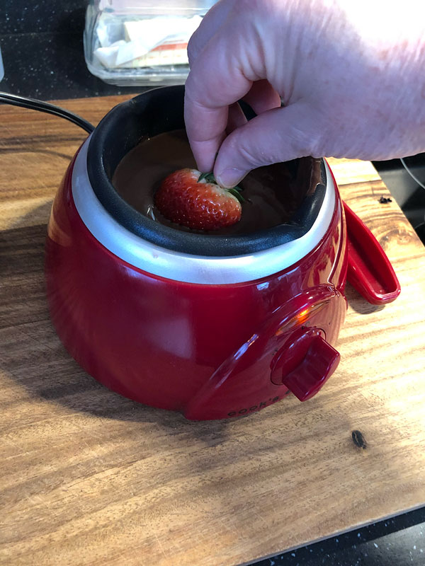 dipping a fresh strawberry in melted chocolate