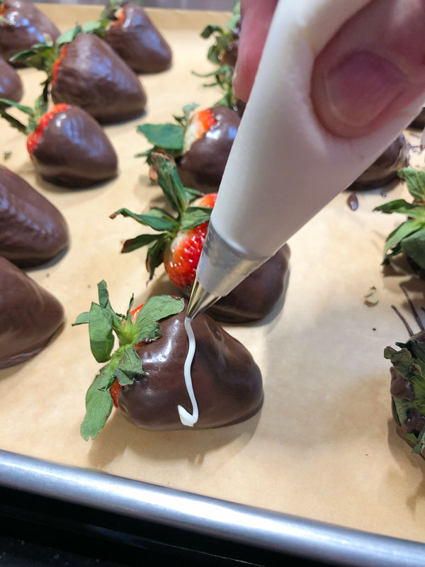 piping white chocolate onto dark chocolate dipped strawberries