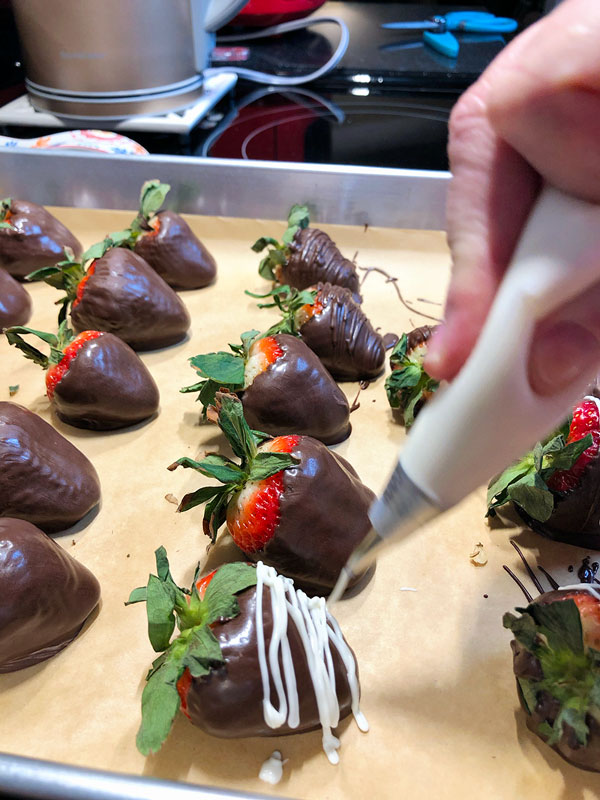 piping white chocolate onto dark chocolate dipped strawberries