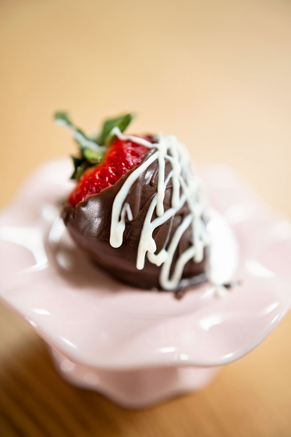 closeup of a strawberry dipped in chocolate and displayed on a pink plate