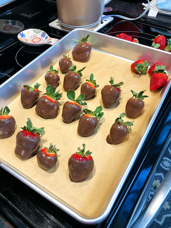 chocolate dipped strawberries sitting on a parchment lined sheet pan