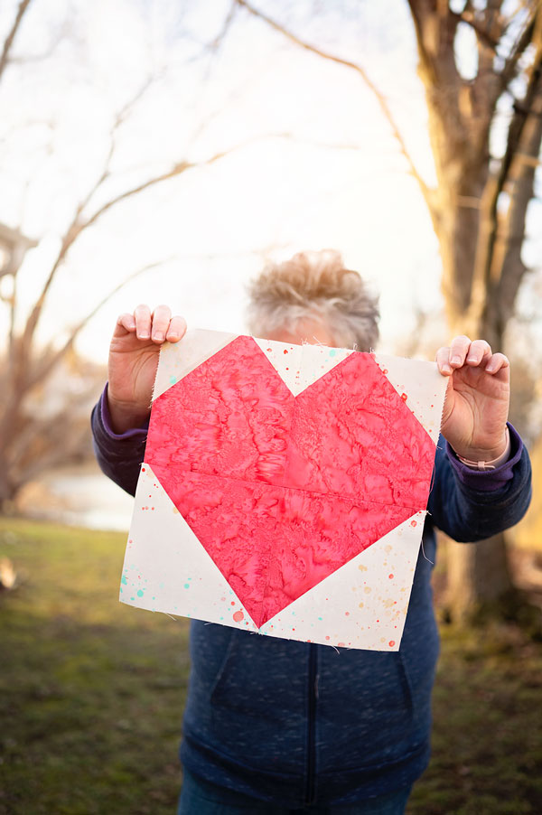 woman holds a pink heart quilt block
