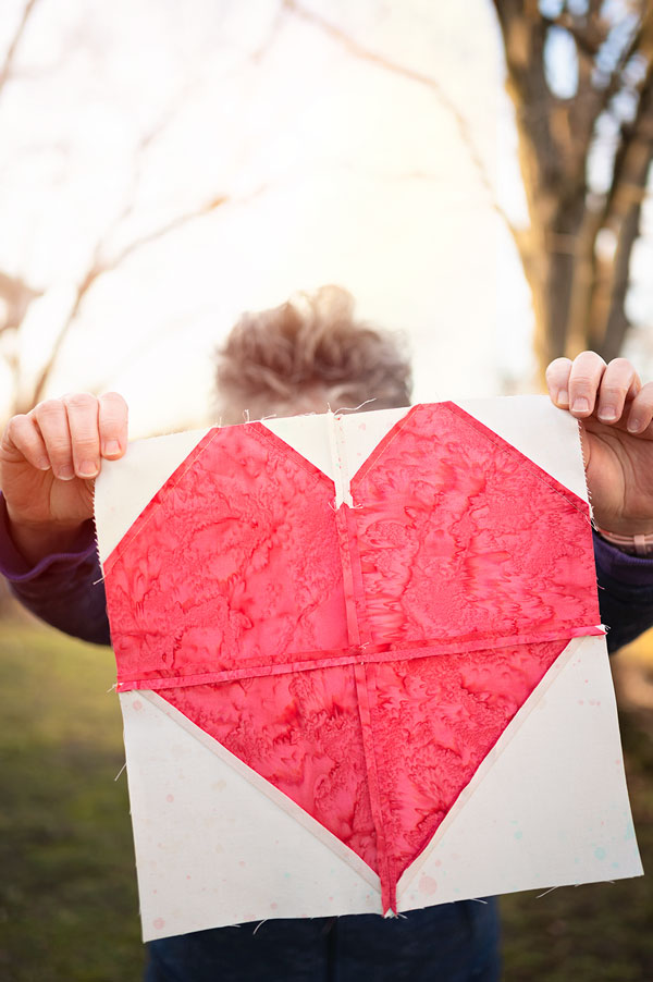 woman holds a pink heart quilt block showing the seams on the back
