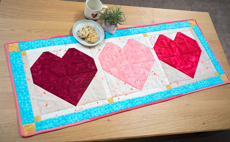 overhead view of a quilted table runner made of 3 colorful hearts