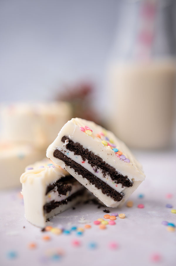 two white chocolate dipped oreos with one cut in half to show the inside