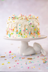 A white frosted cake decorated with colorful sprinkles on a cake plate that looks like a bunny