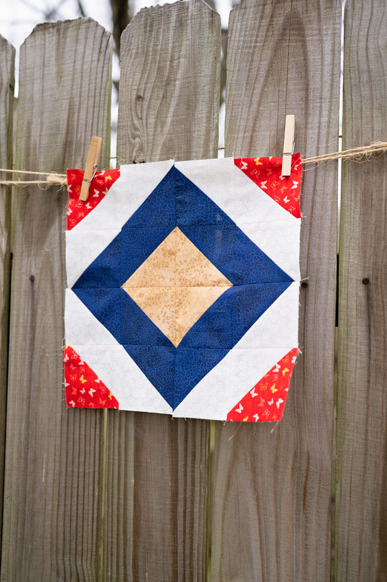 a diamond quilt block hangs on a rustic fence