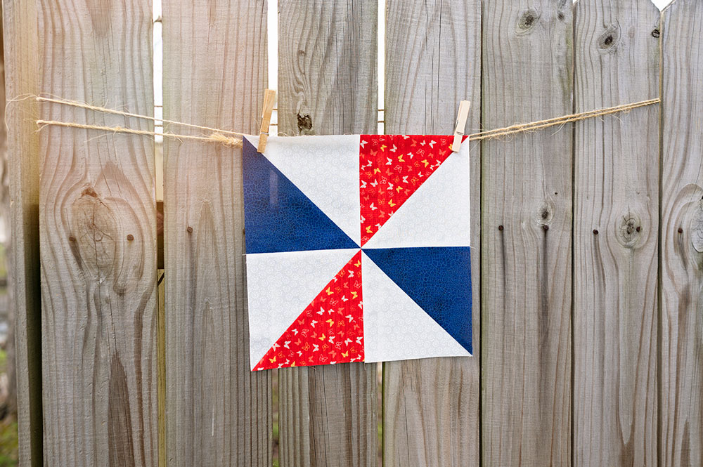 a pinwheel quilt block hanging on a rustic fence