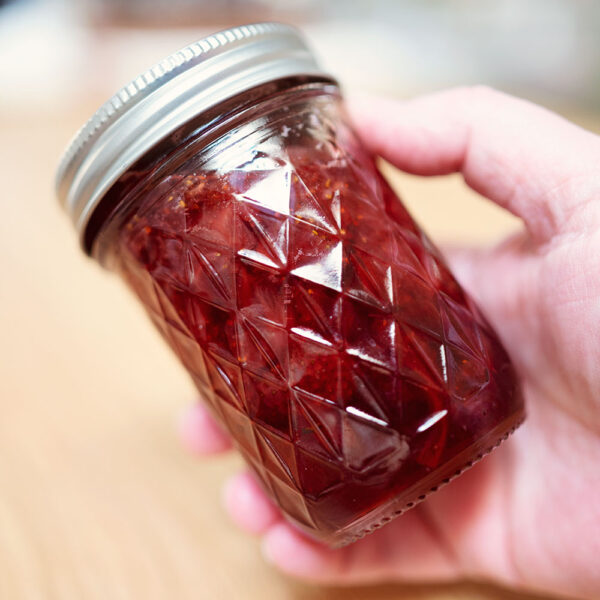 hand holds a small jar of strawberry jam