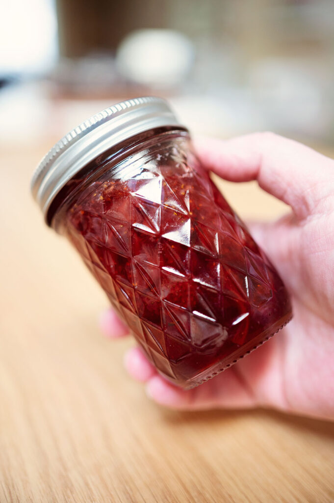 hand holds a small jar of strawberry jam