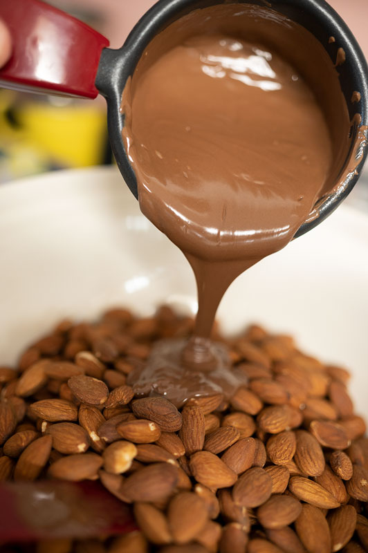 pouring melted chocolate over roasted almonds
