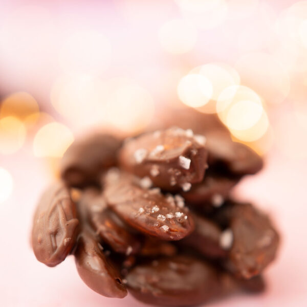 a cluster of chocolate covered almonds on a pink background with fairy lights and surrounded by crumbs of almonds.