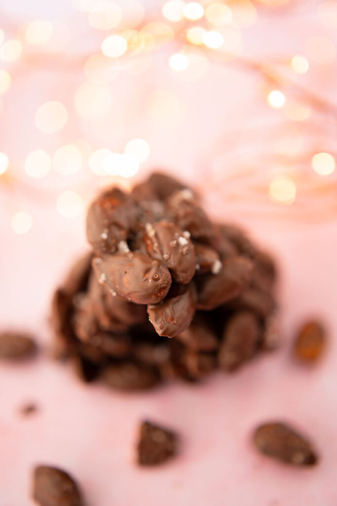 a cluster of chocolate covered almonds on a pink background with fairy lights and surrounded by crumbs of almonds.