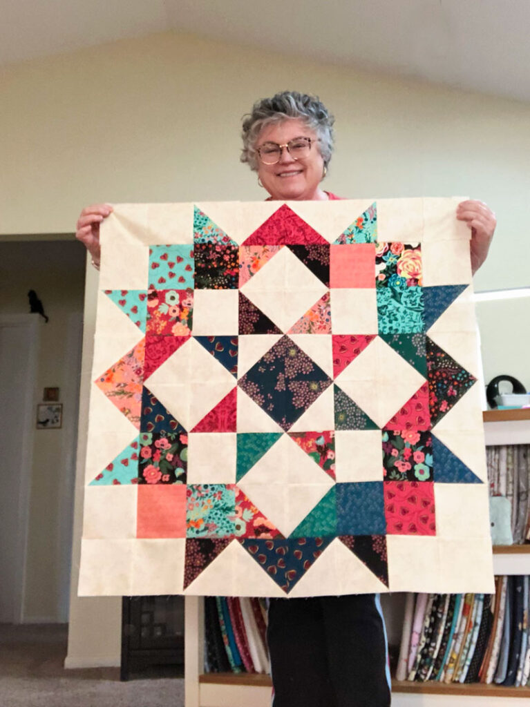 smiling woman holds a large quilt block
