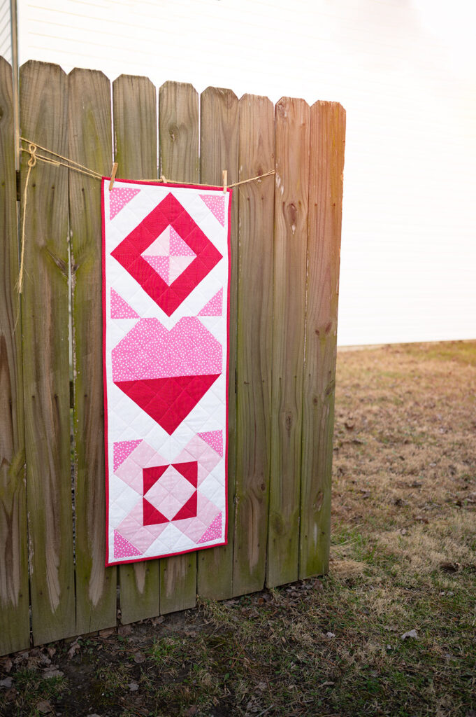 modern quilted table runner celebrating valentine's day displayed on a rustic fence