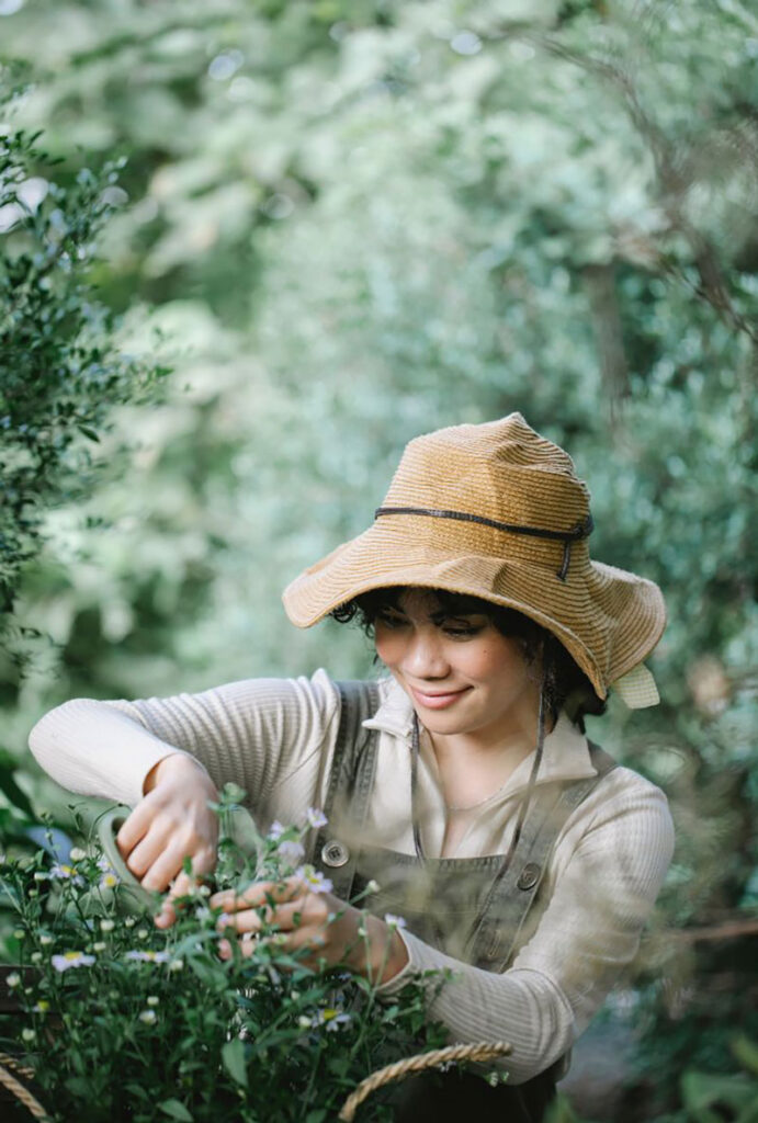 woman in a floppy garden hat is pruning herbs