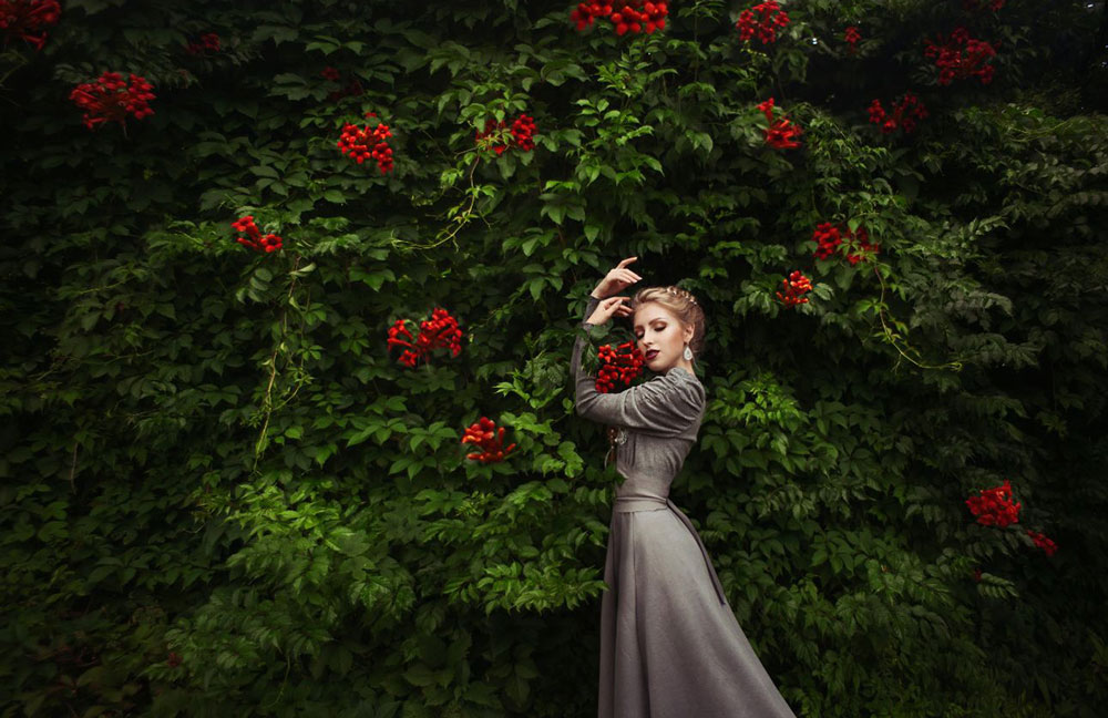 woman in long gown poses with large flowering hedges