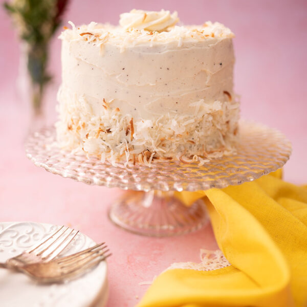 a white layer cake on a cake stand with a sunshine yellow linen napkin