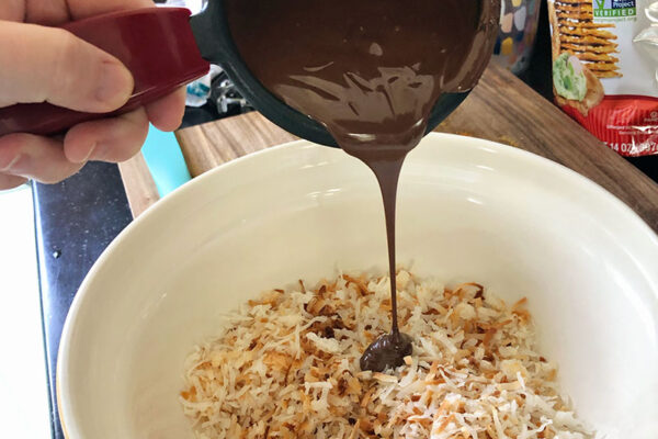 pouring melted chocolate over cooled, toasted coconut