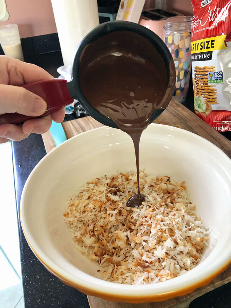 pouring melted chocolate over cooled, toasted coconut