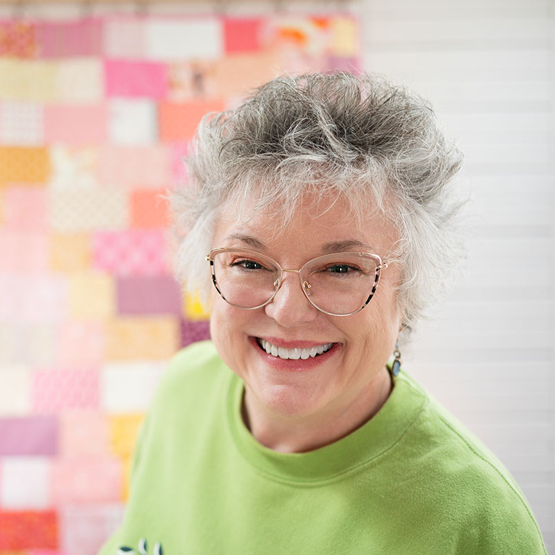 smiling woman in a bright green shirt with a pink patchwork quilt
