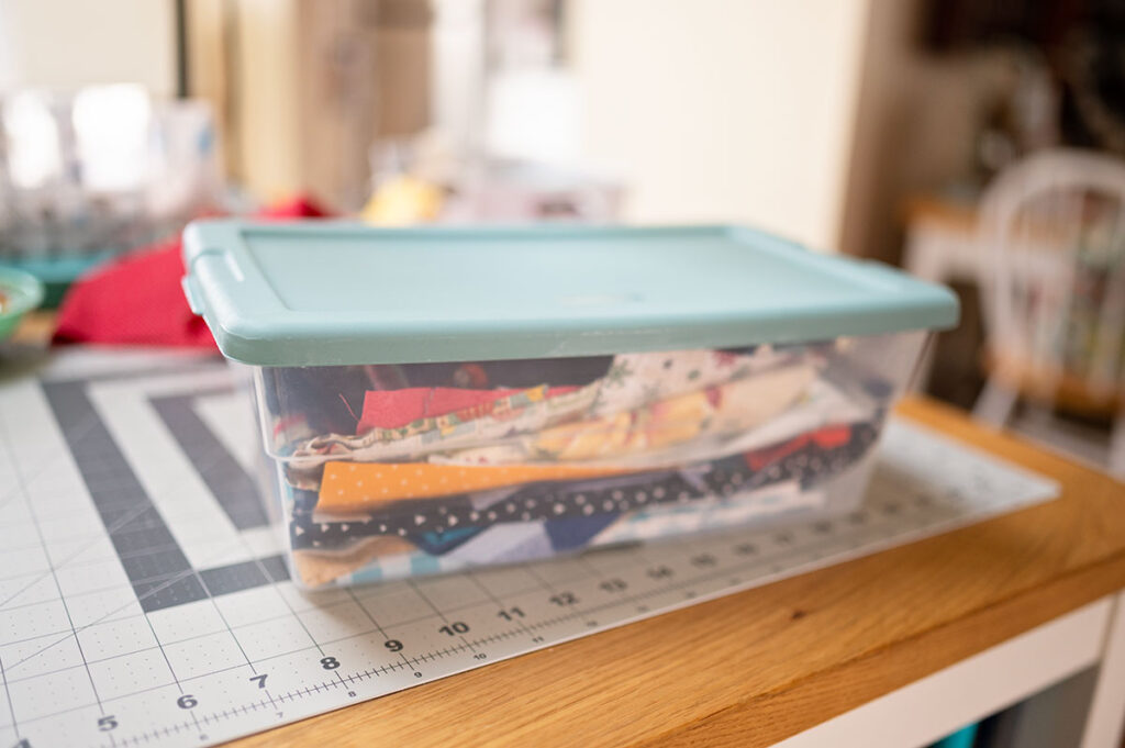 a plastic container on a table top fill with colorful scraps of fabric