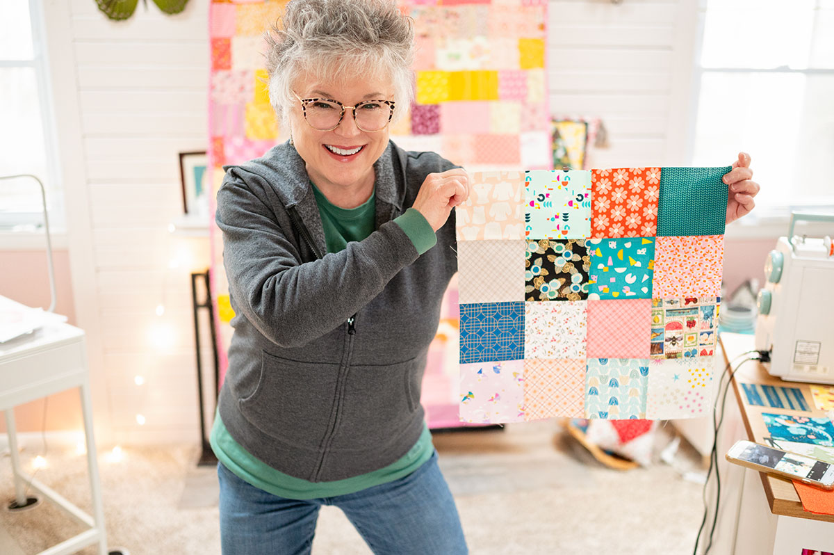 a smiling woman holds a large scrappy quilt block