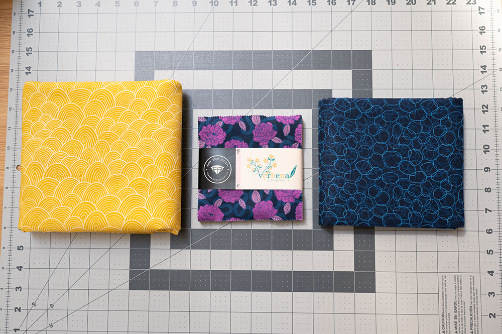 two colorful printed fabrics with a charm pack of fabric