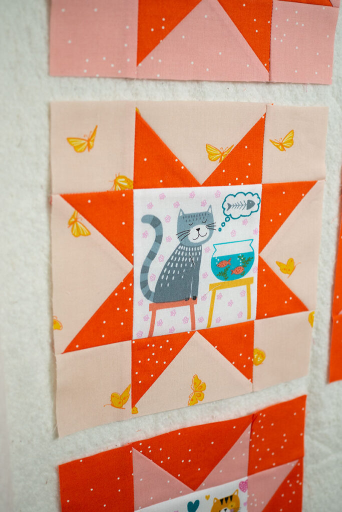 cream and orange sawtooth star quilt block with illustrated cats in the center