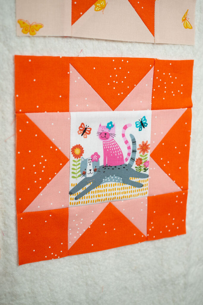 pink and orange sawtooth star quilt block with illustrated cats in the center