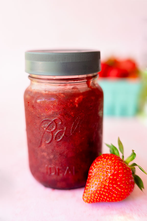Classic Ball pint jar filled with fresh strawberry jam and topped with a leak proof lid and fresh strawberry